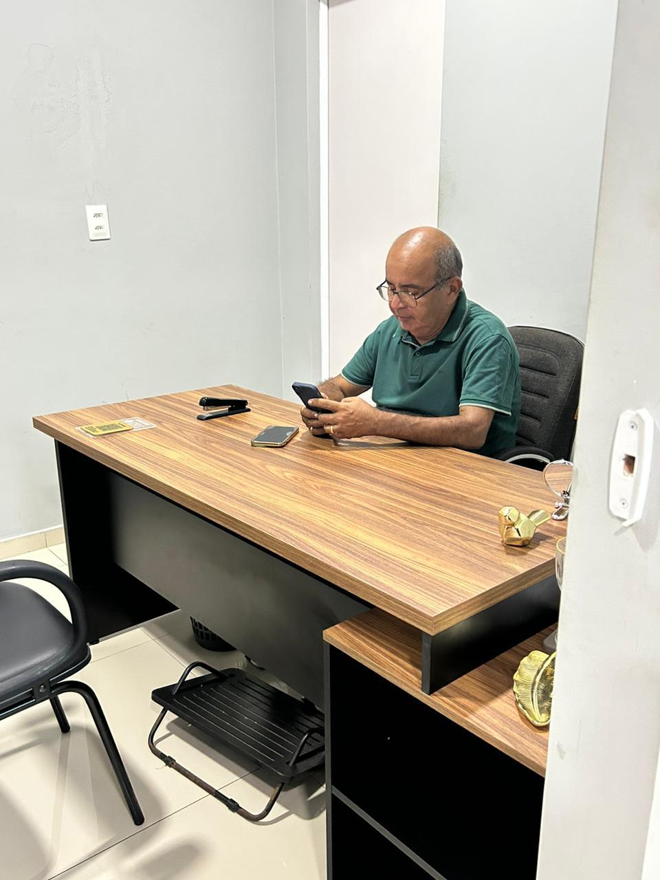 Homem sentado à mesa no escritório durante atendimento pelo celular.